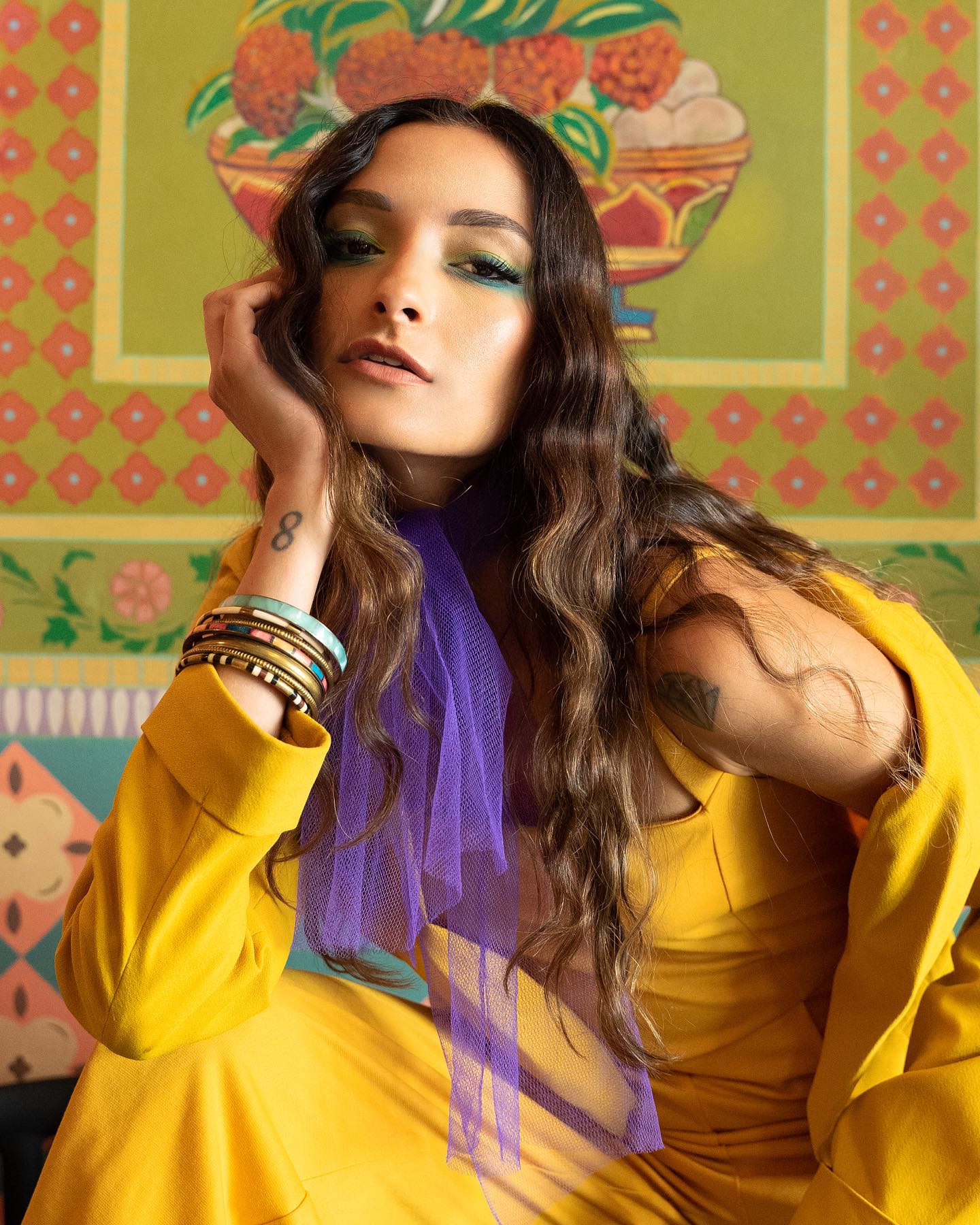 Rafaela in a yellow suit and purple tulle scarf, green eyeshadow, in front of a hand-painted Indian floral mural — agency editorial shoot, October 2023.
